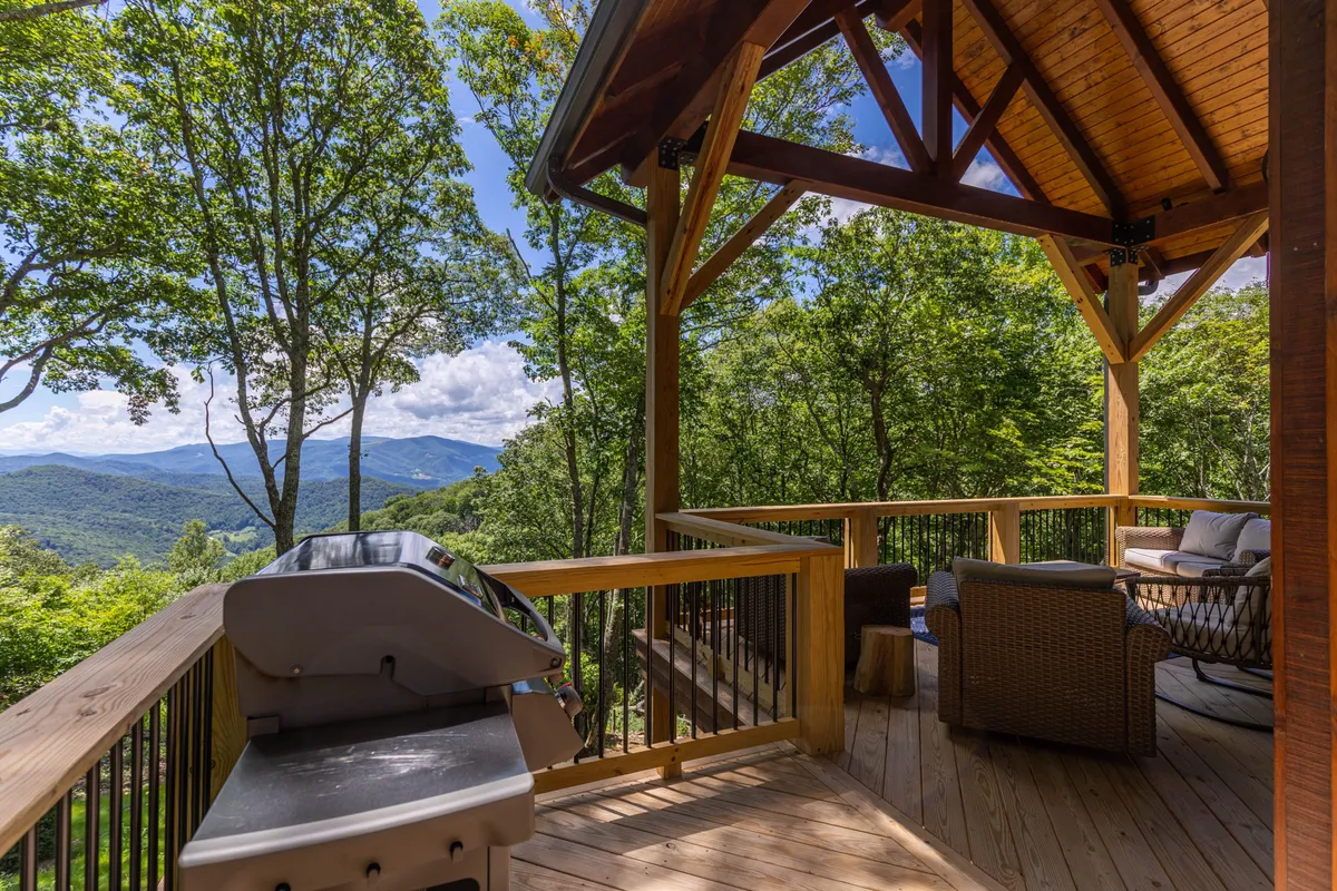 An outdoor seating area with a grill set against a backdrop of distant mountains and lush greenery, offering a serene spot to enjoy nature, barbecue, and watch dogs play in a safe, open-air environment.