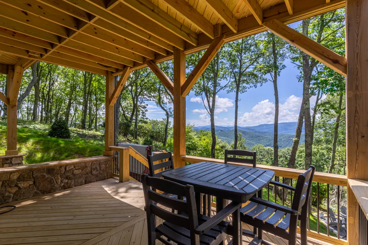 A wooden deck perched above lush greenery, with a dining table set for outdoor meals and panoramic mountain vistas beyond. The scene captures serene moments from morning coffee to family gatherings, all with a backdrop of the stunning Blue Ridge Mountains.