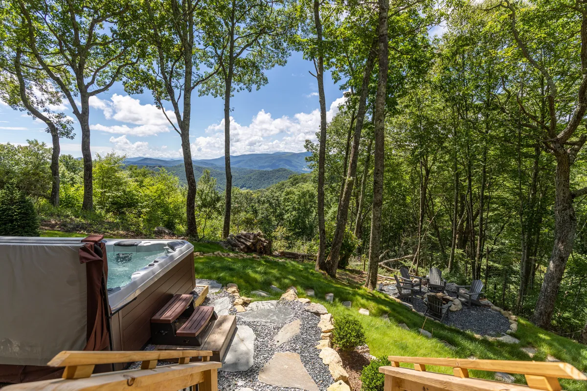 This image showcases a private hot tub situated on a patio, overlooking the scenic Blue Ridge Mountains. The seating area and surrounding lush greenery create an inviting atmosphere for relaxation and socializing while taking in the expansive mountain views.