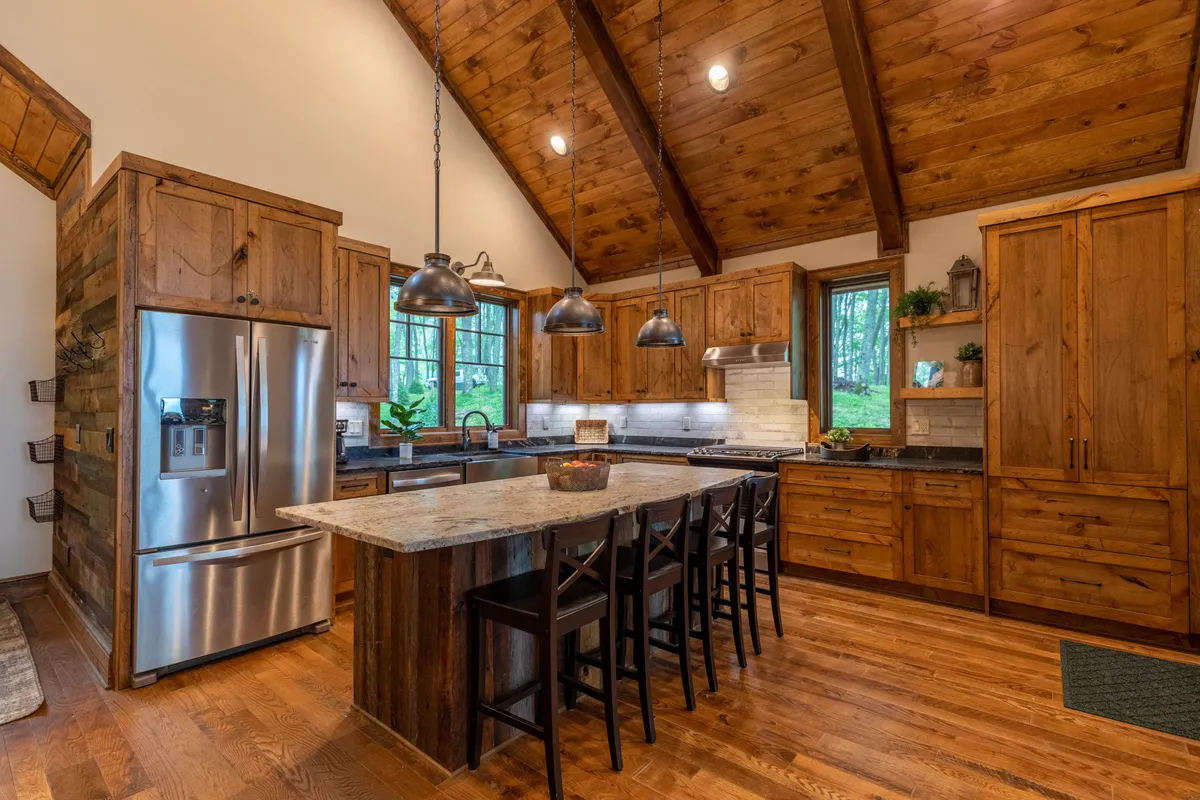 A gourmet kitchen featuring a spacious island countertop, gleaming stainless steel appliances, rich wood cabinetry, and oversized windows filling the space with daylight. The layout is open, seamlessly connecting to adjacent living and dining areas—ideal for both cooking and entertaining.