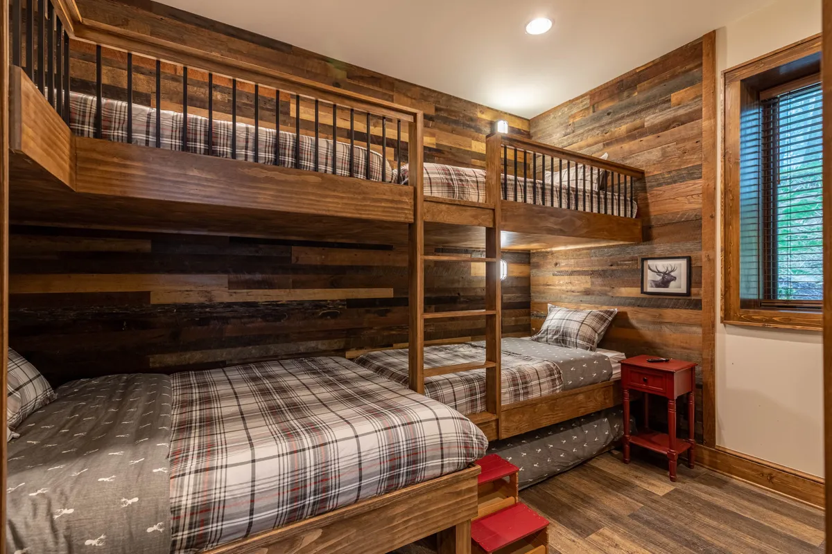 A playful yet inviting bunk room with bunk beds, plaid bedding, a wooden wall, and a bright red nightstand. The space is designed for comfort and fun, perfect for children to enjoy their own private enclave.