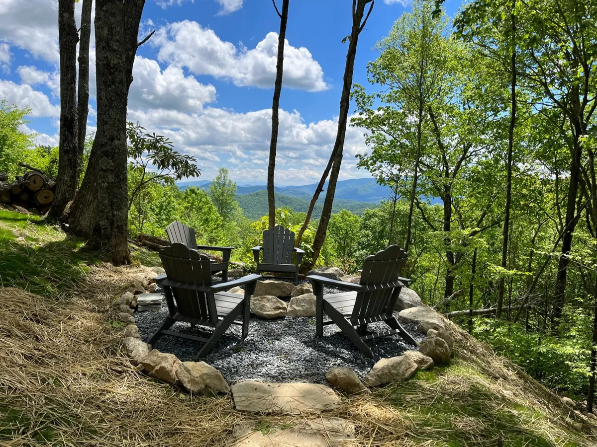 A stone-ring fire pit encircled by four Adirondack chairs, set in a natural landscape with expansive mountain views. The scene evokes evenings spent around a crackling fire, sharing stories, roasting s’mores, and enjoying the tranquility of the outdoors.